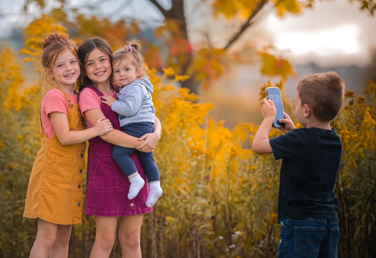 Three sisters posing together while their brother takes a photograph outdoors