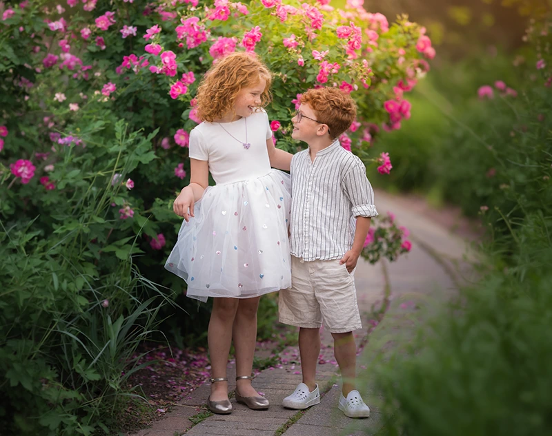 Brother and sister smiling together beside bright pink flowers