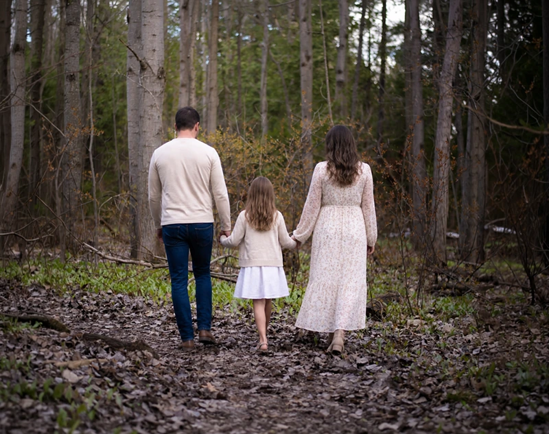 Parents and their daughter walking hand in hand along a wooded trail